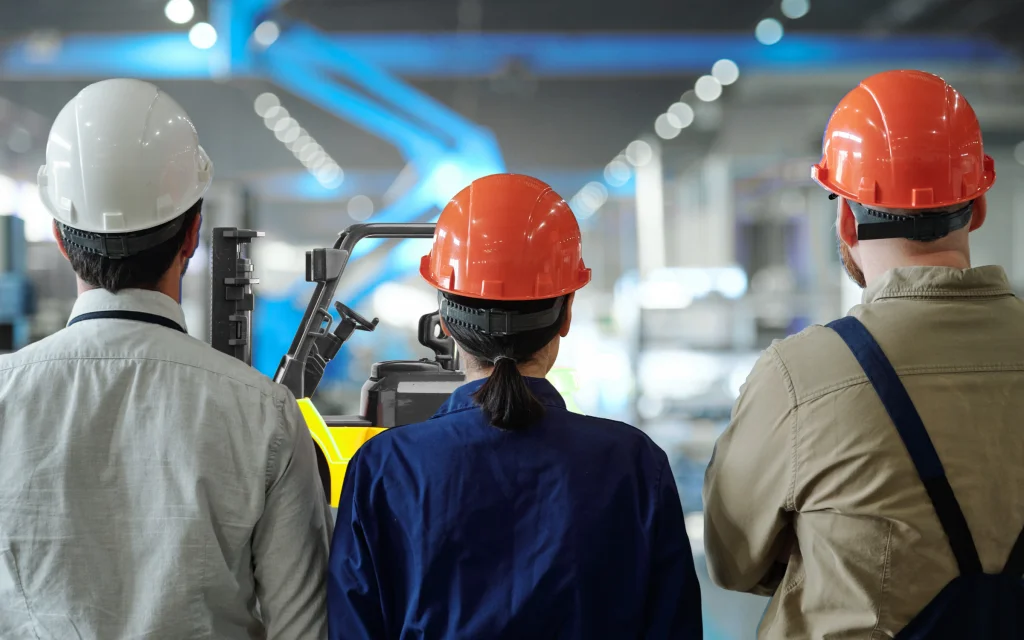 Industrial workers observing forklift operations in a manufacturing facility, illustrating proactive safety practices, hazard awareness, and the shift beyond lagging indicators in safety.