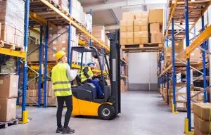 Connected safety technology in a material handling warehouse with a forklift transporting inventory and workers operating near industrial storage racks.