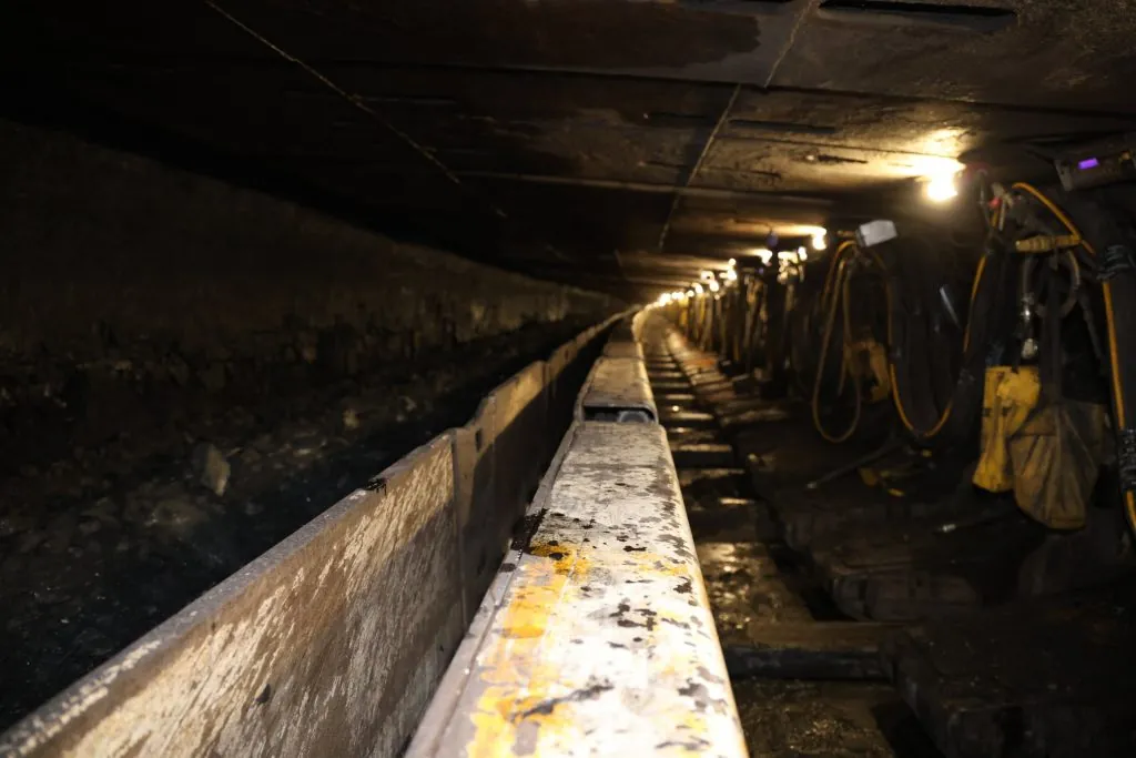Underground longwall coal face showing a line of hydraulic roof shields and the face conveyor under mine lighting at Tunnel Ridge.