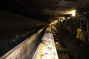 Underground longwall coal face showing a line of hydraulic roof shields and the face conveyor under mine lighting at Tunnel Ridge.